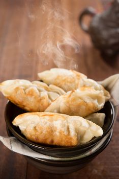 Fresh pan fried dumplings on bowl. Chinese dish with hot steams on rustic vintage wooden background. 