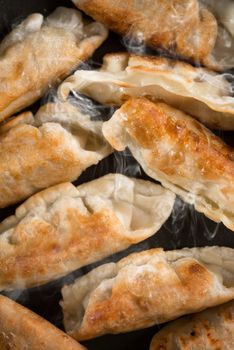 Close up cooking fried dumplings in a frying pan. Chinese cuisine with hot steams, on rustic vintage wooden background. 