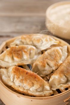 Fresh pan fried dumpling on bamboo basket. Chinese food with hot steams on rustic vintage wooden background. 
