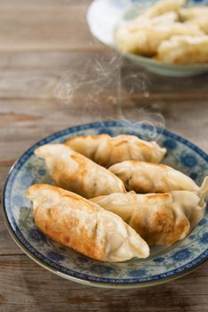Fresh pan fried dumpling on plate. Chinese food with hot steams on rustic vintage wooden background. Fractal on the plate is generic print.