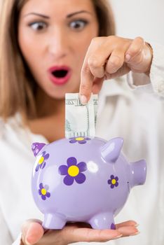 Close-up of a businesswoman hand putting money in piggy bank. Saving and financial concept. Selective focus. Focus on piggy bank, on foreground.