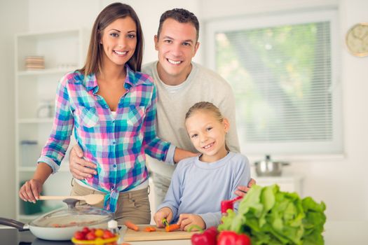Cheerful beautiful family enjoying while preparing food in the kitchen. Looking at camera.