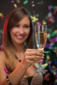 Close-up of a beautiful woman holding with champagne. Focus on foreground, on champagne. Confetti is the air.