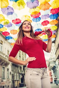 Beautiful young woman with red umbrella walking down the street decorated with lots of multicolor umbrellas.