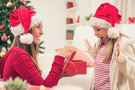 Beautiful young mother surprise their cute little girl with Present for Christmas or New Year. 