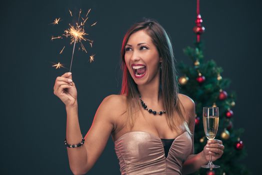 Cheerful beautiful woman celebrating New Year. She is having fun with sparkler and champagne.
