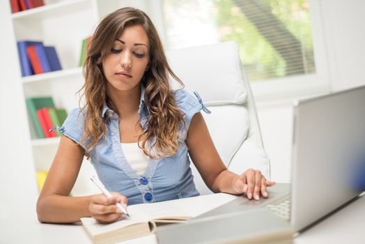 Beautiful teenage girl with book and laptop learning in the library.