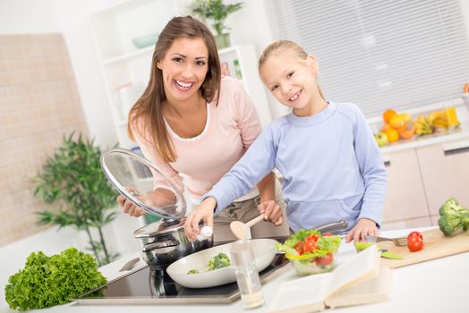 Young beautiful mother and her cute daughter cooking healthy meal in the kitchen.