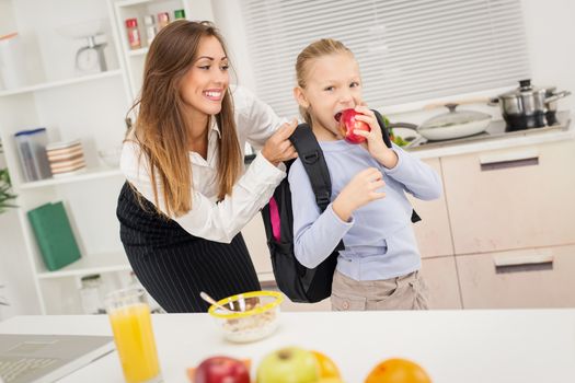 Young beautiful mother preparing her cute daughter for school.