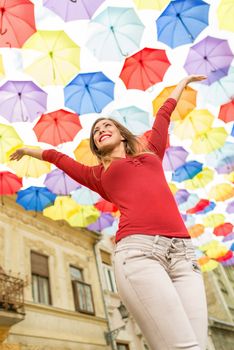 Cheerful beautiful young woman in the street decorated with lots of multicolor umbrellas.