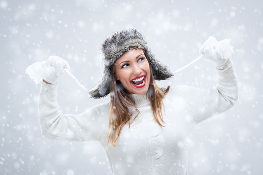 Cheerful beautiful young woman in warm clothing having fun while snowing.