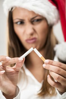 Close-up of a beautiful young woman wearing santa hat and breaking cigarette. Selective focus. Focus on foreground, on cigarette.