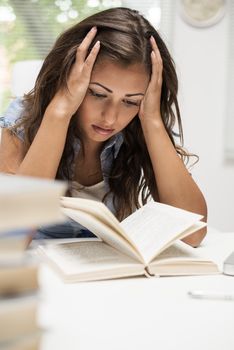 Portrait of tired beautiful teenage girl holding her head and learning.