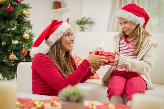 Cute little girl giving a present to her mother for Christmas or New Year. 