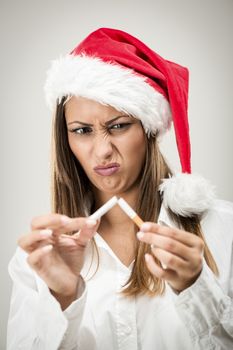 Portrait of a beautiful young woman wearing santa hat and breaking cigarette.