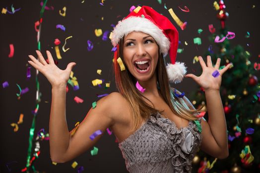 Cheerful beautiful woman celebrating New Year. She is having fun, confetti is in the air.