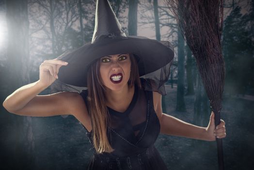 Young woman dressed like a witch. She is in dark clothing and holding a broom.