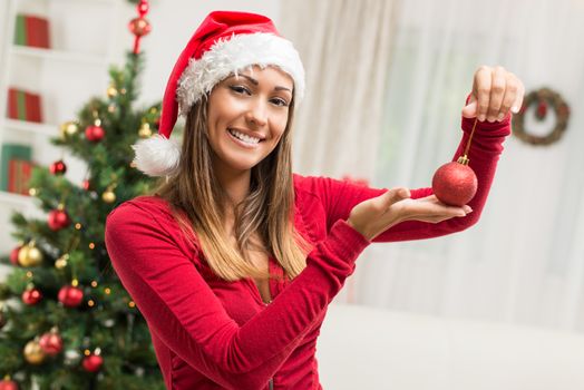 Happy beautiful young woman holding red Christmas ornament