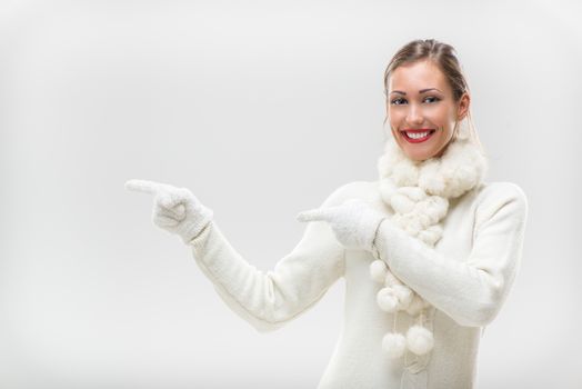 Beautiful young woman in winter clothes pointing to something besides itself with outstretched fingers.