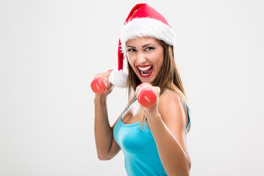 Beautiful fitness woman wearing santa hat doing exercise training arms lifting dumbbells.