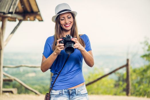 Young beautiful woman standing by viewpoint and looking photography on the digital camera.