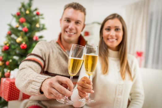 Romantic young couple toasting with champagne home interiors at christmas time.  Selective focus. Focus on foreground.