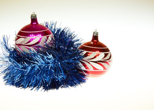 Two red Christmas balubles, one wrapped in a decorative blue chain and one on her right side. The whole on an isolated white background