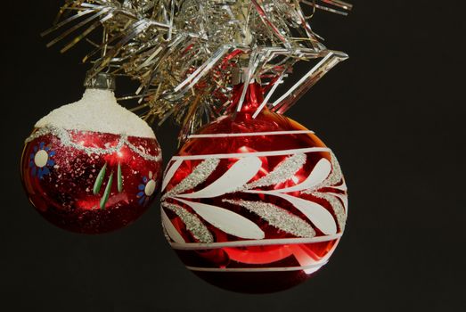 Two red Christmas balls with ornaments of imposed from the top of an ornate silver chain. The whole on a black isolated background