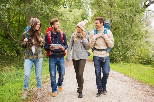 adventure, travel, tourism, hike and people concept - group of smiling friends with backpacks and map walking outdoors