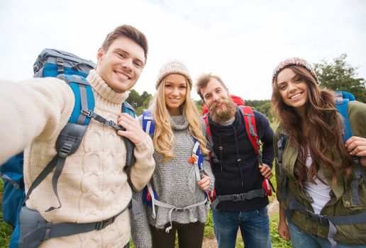 adventure, travel, tourism, hike and people concept - group of smiling friends with backpacks making selfie outdoors