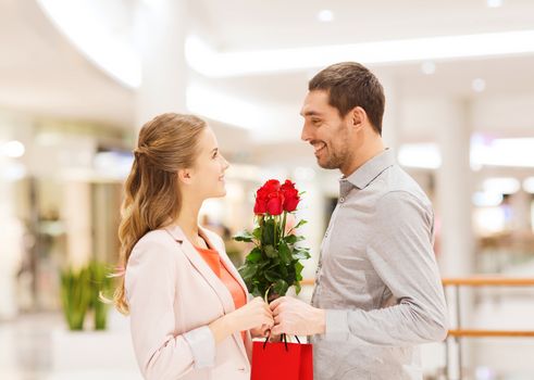 relations, love, romance and people concept - happy young couple with flowers talking in mall