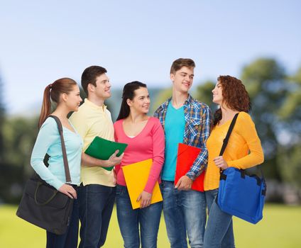 friendship, vacation, education and people concept - group of smiling teenagers with folders and school bags over park background