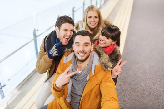 people, friendship, technology and leisure concept - happy friends taking selfie with camera or smartphone on skating rink