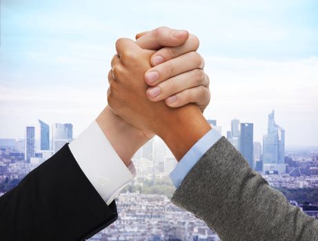 business competition, challenge, cooperation, people and partnership concept - concept - close up of hands arm wrestling over city background