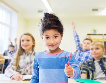 education, elementary school and children concept - happy little student with pen girl over classroom and classmates background