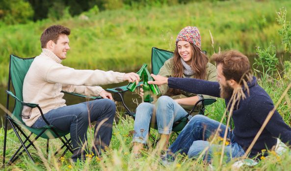 adventure, travel, tourism, friendship and people concept - group of smiling tourists clinking beer bottles in camping