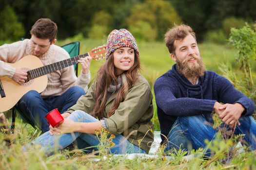 adventure, travel, tourism and people concept - group of smiling friends with guitar in camping