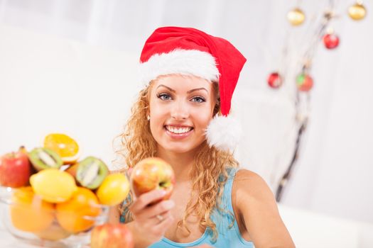 Beautiful young woman on New Year's day  eat apple in her home with Santa Hat