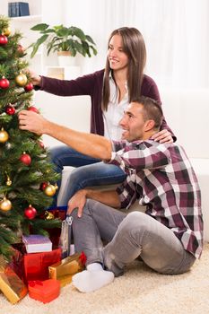 Happy young couple enjoy decorating Christmas tree at home.