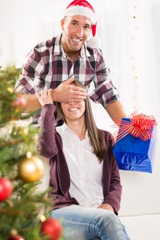 Young man gives his girlfriend a Christmas gift her hand over her eyes.