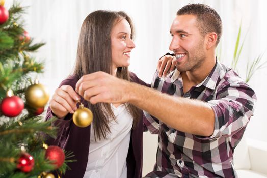 Happy young couple enjoy decorating Christmas tree at home.