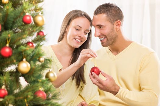 Happy young couple enjoy decorating Christmas tree at home.