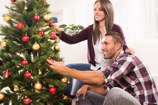 Happy young couple enjoy decorating Christmas tree at home.