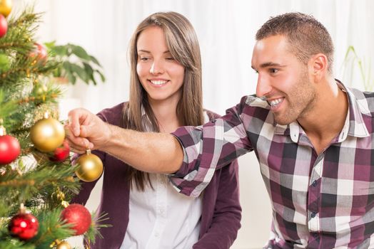 Happy young couple enjoy decorating Christmas tree at home.