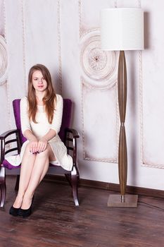 Attractive young woman sitting  in a chair next to a floor lamp. Vertical shot.