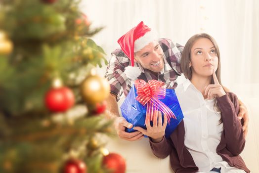 Young man gives his girlfriend a Christmas gift. She is conceived and looking up.