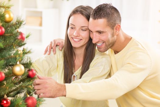 Happy young couple enjoy decorating Christmas tree at home.