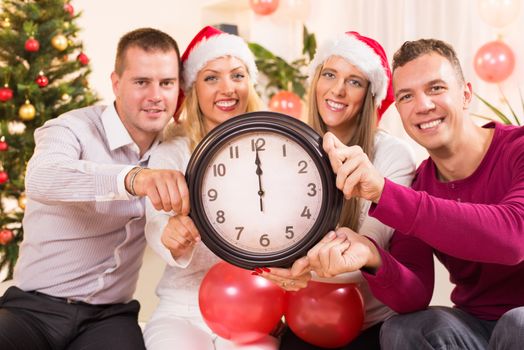 Happy friends Celebrating New Year in home interior and showing midnight on the clock. Selective Focus, focus on the clock.