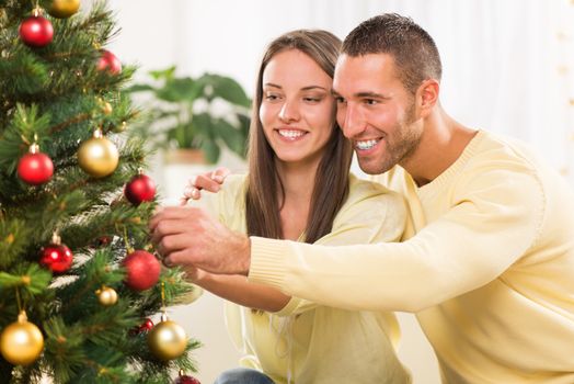 Happy young couple enjoy decorating Christmas tree at home.