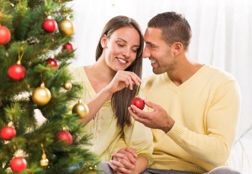 Happy young couple enjoy decorating Christmas tree at home.